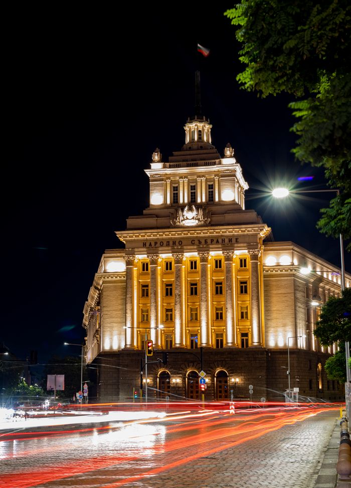Striking night view of a grand lit government building with car light trails in the foreground.
