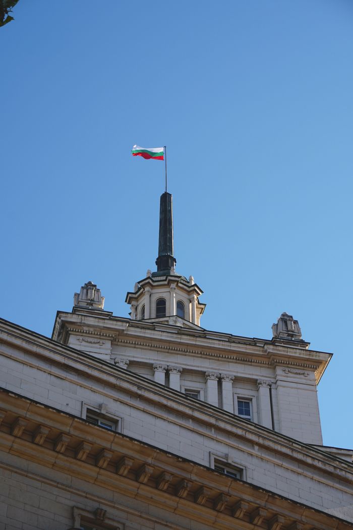 Bulgarian National Assembly building with flag under clear blue sky.